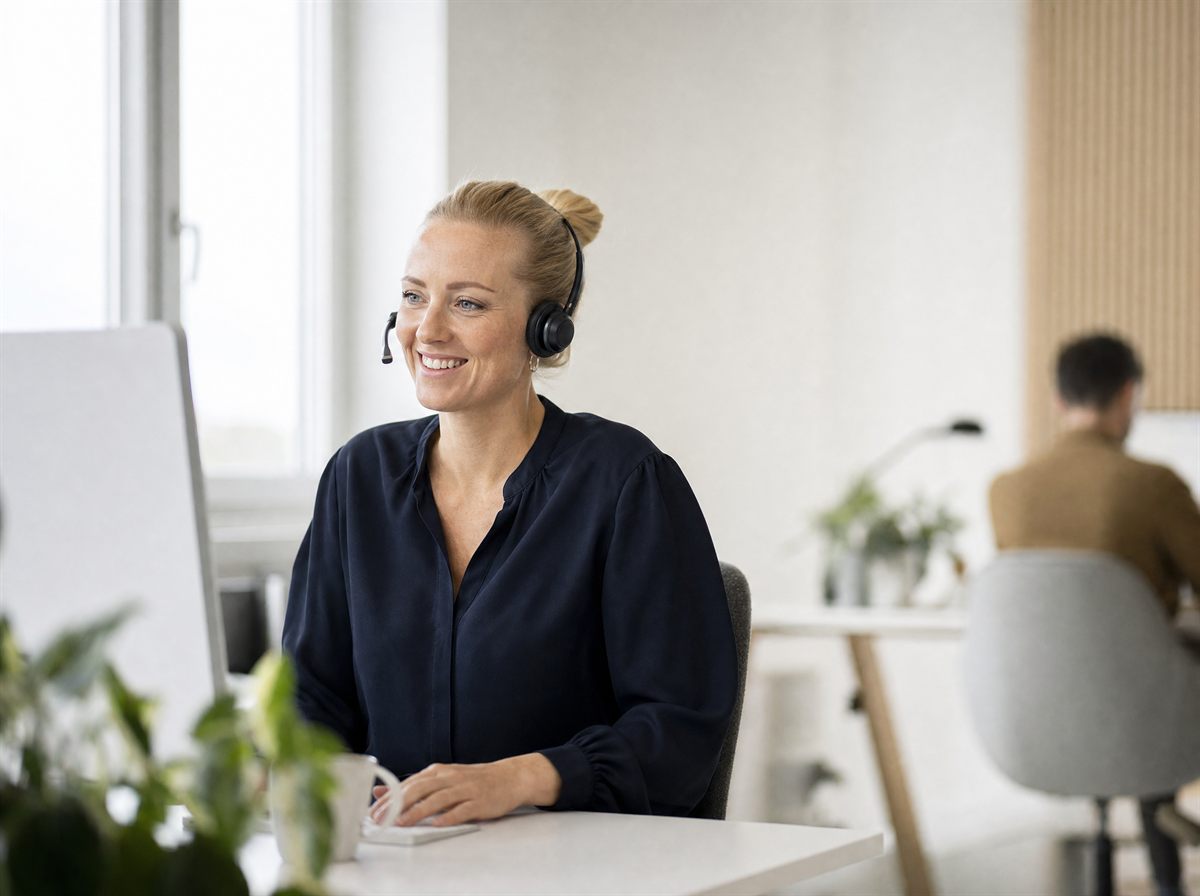 Kundeservicemedarbeider med headset på et lyst kontor svarer på en henvendelse